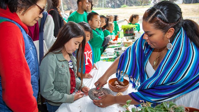 Ranger dressed in a traditional Latina outfit demonstrating making tortillas to visitors