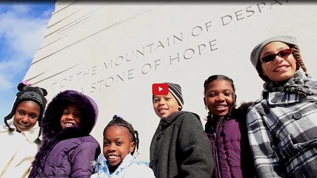 Teacher and students standing below an engraved Dr. King quote on a statue 