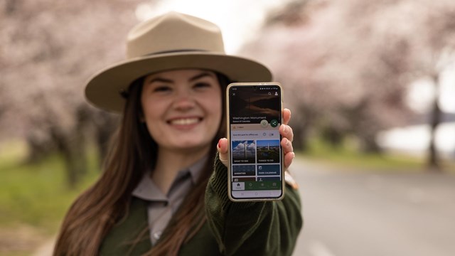 Ranger holiding up a phone with displaying the app 