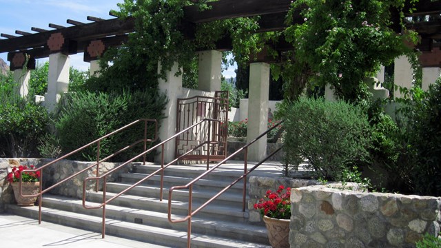 A stone stairway leading to a gate lined by green vines and bushes.