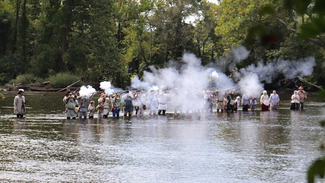 A group in costume fire historic weapons while standing in a river.