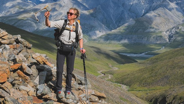 Woman holding GPS collar above her head while standing on a mountain top