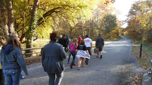 Photo of a group of people walking on a paved road with trees in the background