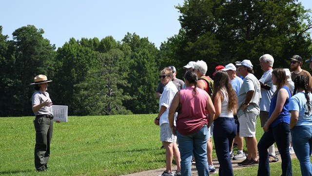 White woman in NPS uniform speaks to a group people on a sunny day.