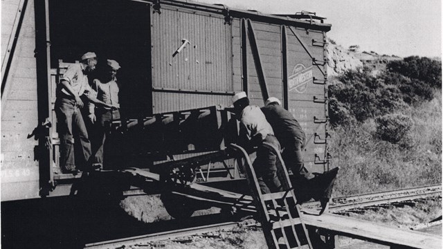 Historic photograph showing four African American sailors loading munitions into a boxcar.