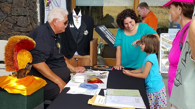 Volunteer demonstrating traditional Hawaiian attire to woman and girl