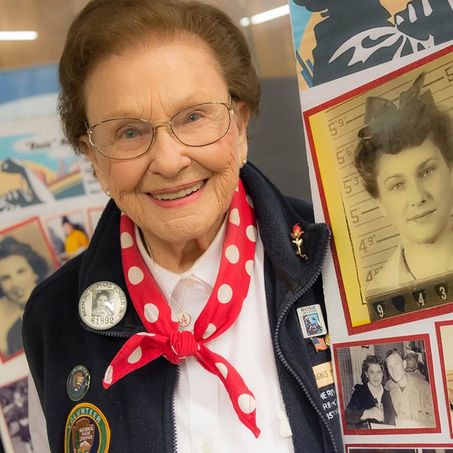 An older woman in an NPS volunteer uniform smiles at the camera.