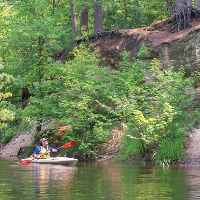 A kayaker paddles past sandstone cliffs.