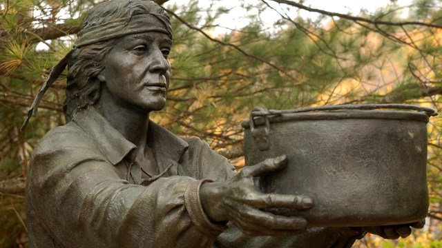 Bronze statue of Passamaquoddy person holding out a basket.