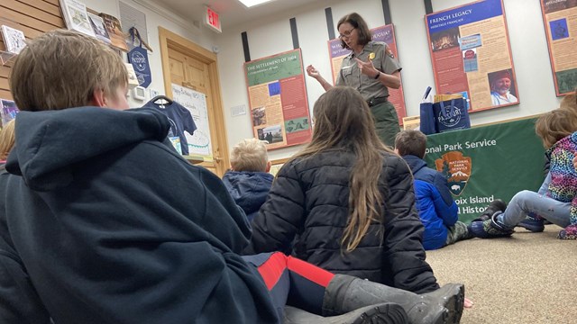 students sit on the floor of the visitor center in front of a park ranger