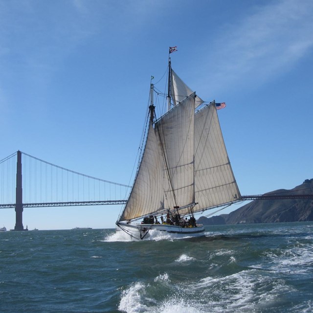 a schooner sails on choppy water with the golden gate bridge in the background