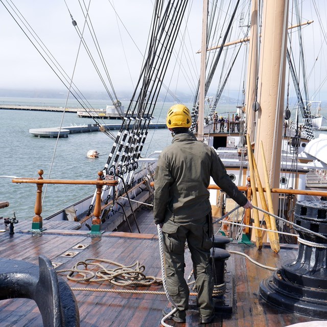 a ranger wearing a hardhat holds line while working on a rigging project on the Balclutha.