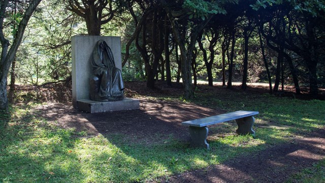 sculpture of shrouded figure with trees and hedges