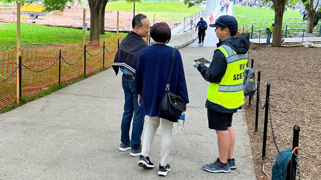 Person in a yellow vest surveys two visitors on a sidewalk