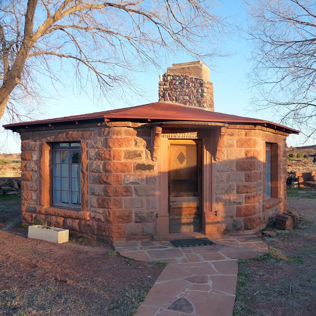 Navajo hogan structure made of stone with a chimney, framed by two bare trees.