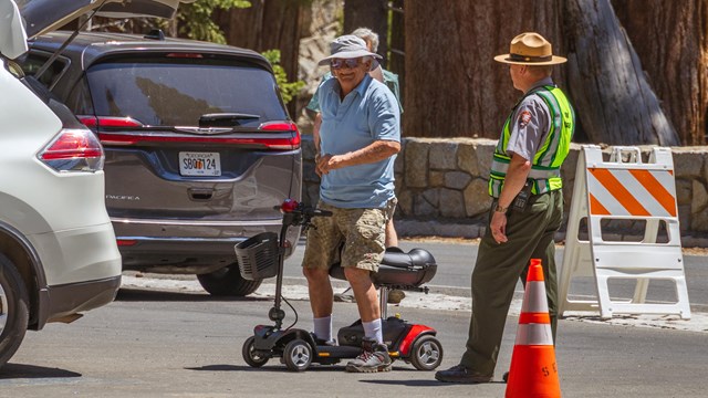 An elderly man standing up from a wheelchair next to a ranger.