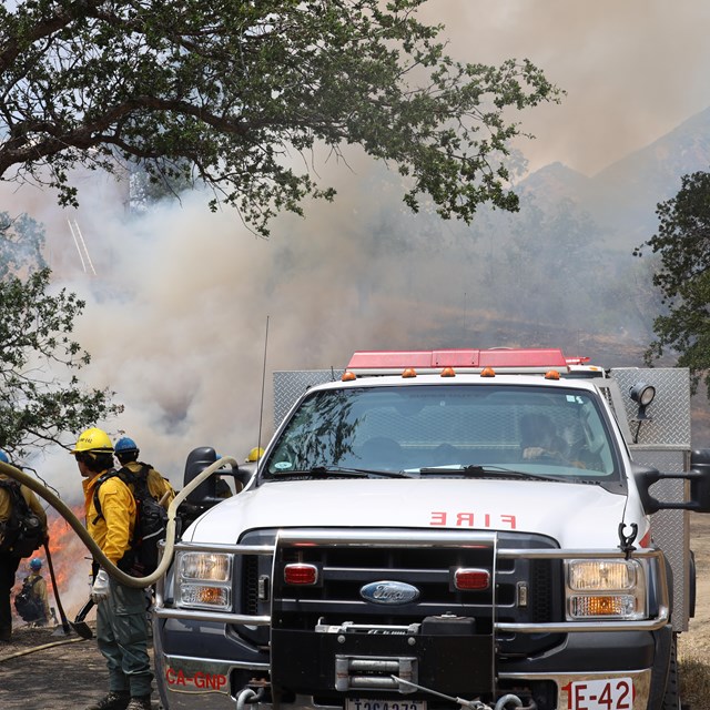 People in yellow shirts and hard hats near a white truck with red striping