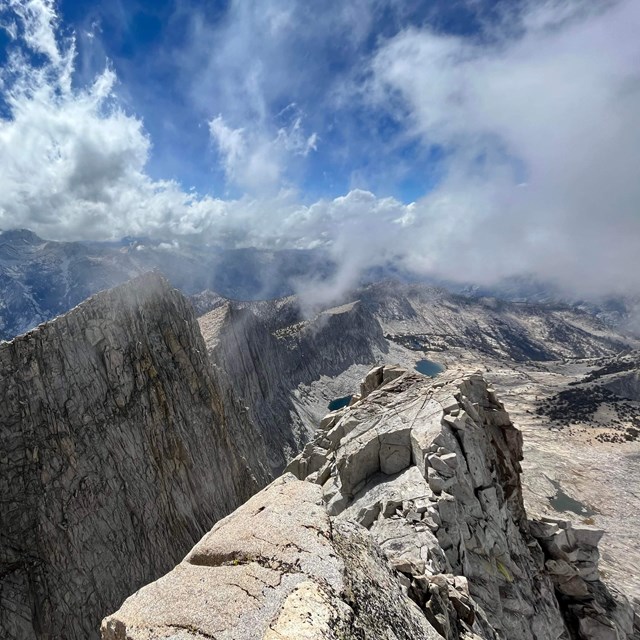 A view from the top of a summit overlooking rocky crags and lakes.