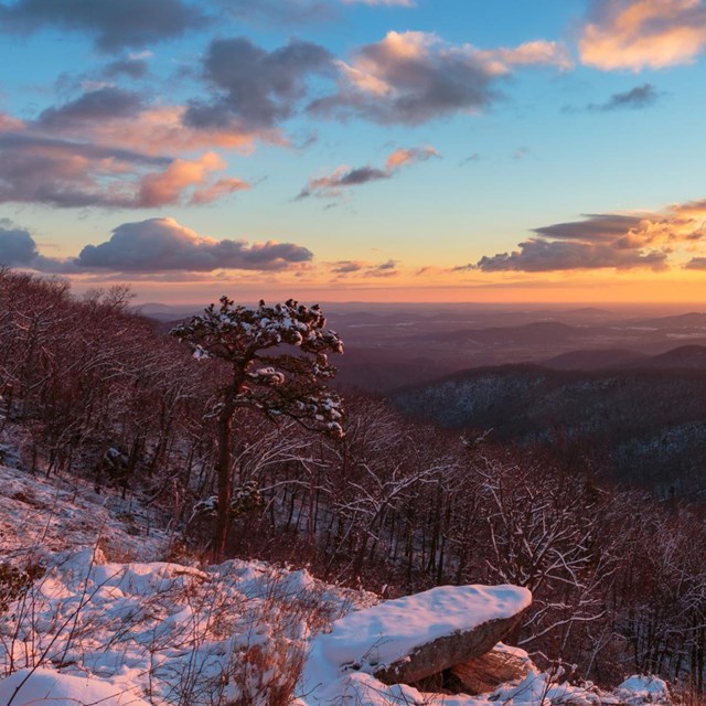 A sunrise behind a mountain layer covered with snow.