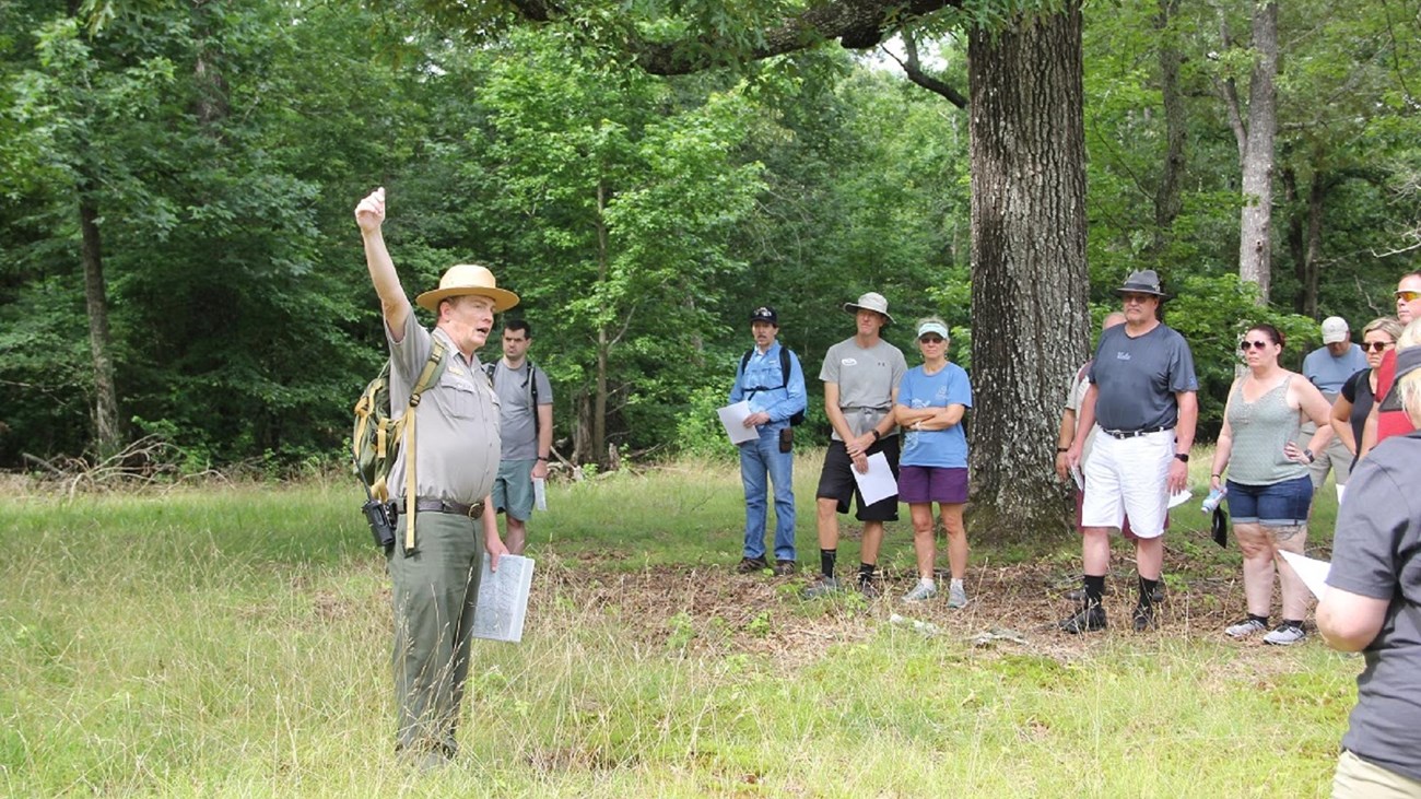 Park ranger in green and gray pointing upward. 