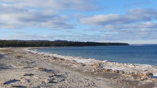 A sandy beach next to a large body of water with ice on the shoreline.