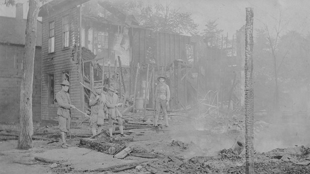 Historic photo of soldiers standing in the burned remains of a building.  