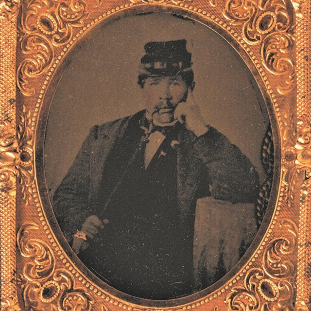 A black and white photo of a Civil War Soldier in uniform smoking a pipe