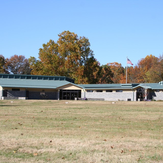 A green roofed building with stone walls and tan sides, with an American flag flying above it.