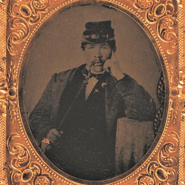 A black and white photo of a Civil War Soldier in uniform smoking a pipe