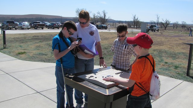 4 visitors gather around 3d map and prepare Trekker Breeze units before hiking the trails.