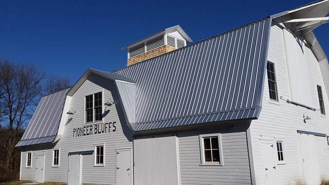 Large white barn with a blue-gray roof reads, "Pioneer Bluffs" above the door.