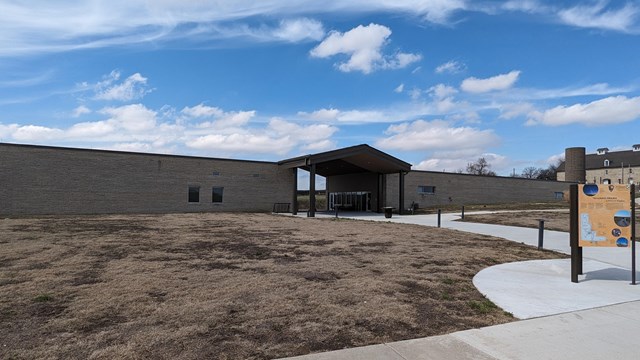 Tallgrass Prairie NP's visitor centers are grey/brown in front of blue sky and brown grass.