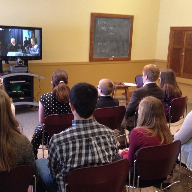 A group of adults watching a tv in a classroom setting