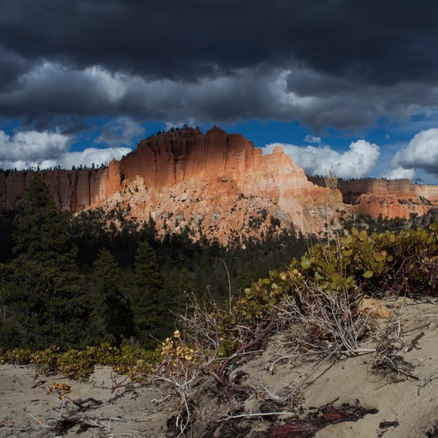 A large land formation with irregular red rock structures under dark storm clouds