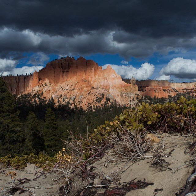 A large land formation with irregular red rock structures under dark storm clouds