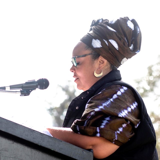 woman in traditional African dress speaking at podium