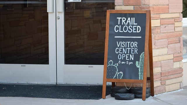 Photo of glass doors with a sign in front of it that says "Trail Closed."