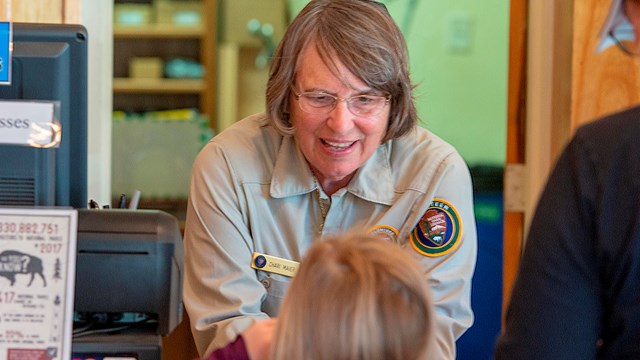 A person in a volunteer shirt talks to a child near a register.