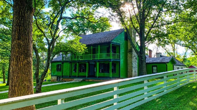 White Fence with Tree in foreground, green house in background.