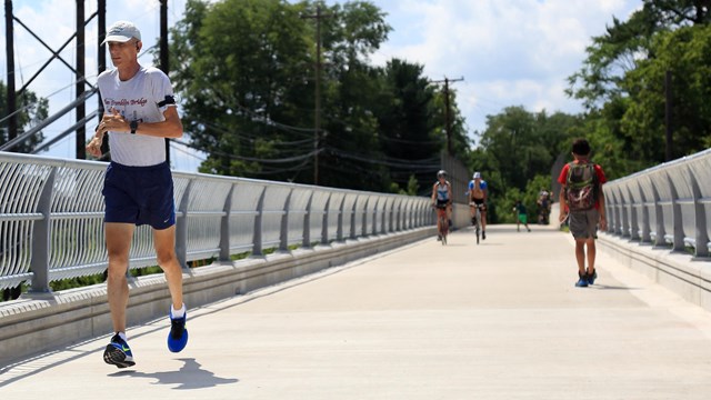 A man runs towards the viewer while a walker headed in the opposite direction passes two cyclists.