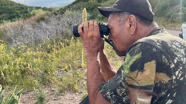 A hunter wearing camouflage, using binoculars to scope out the landscape.