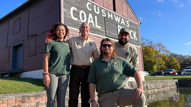 Four volunteers pose for a photo on a dock in front of a wooden building.