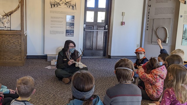 A ranger with several children sitting in a semi circle.