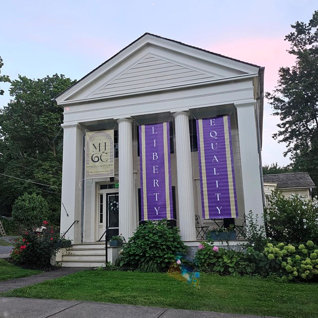 A large white house with purple banners hanging from the porch