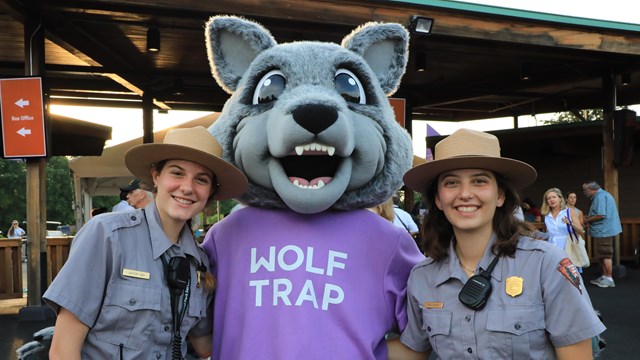 Two female rangers and a wolf mascot pose.