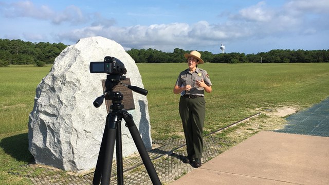 color photo of ranger on left and young girl on right wearing a ranger hat next to a statue of a man