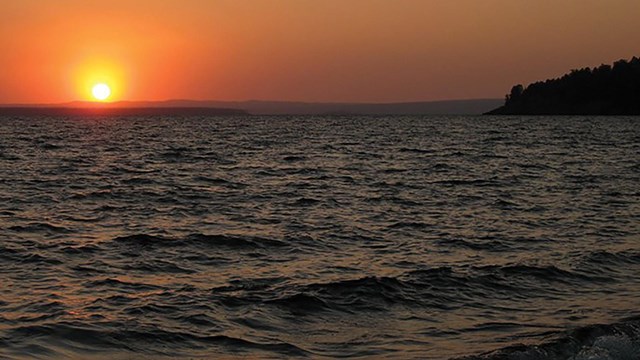 Sunset turns the sky a bright orange as waves lap against the lakeshore.