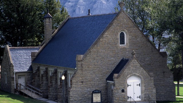 The grey stone chapel at Mammoth Hot Springs surrounded by green grass.