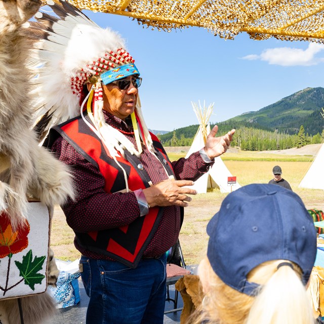 a person wearing traditional Native American regalia speaking to visitors