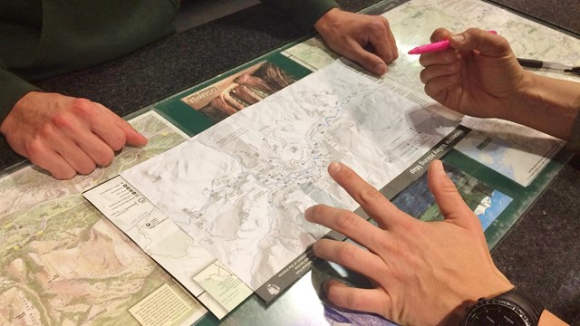 Ranger and visitor hands and trip planning materials at visitor center desk